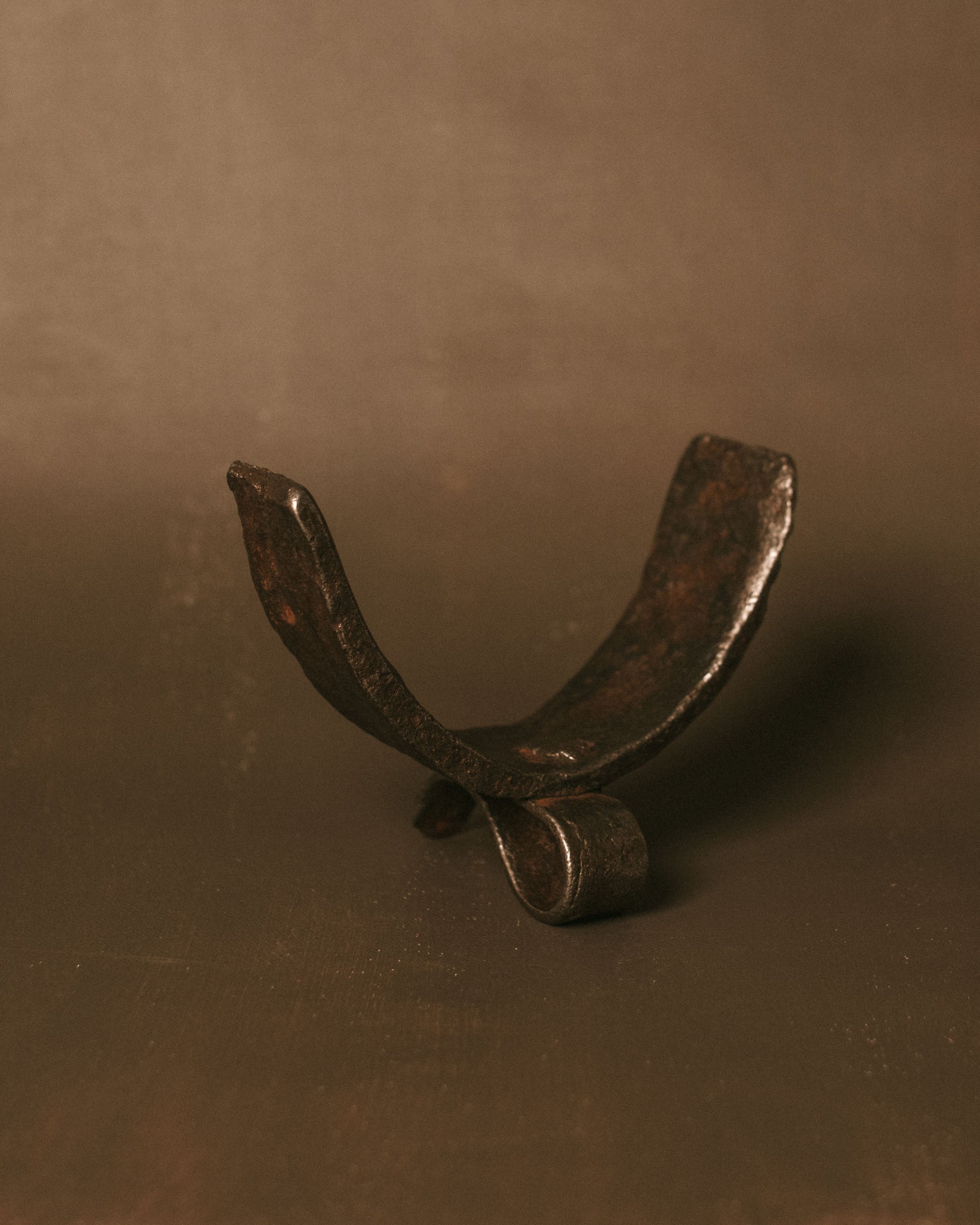 Horn-shaped found iron object with curved form and dark patina, displayed as a small sculptural piece.