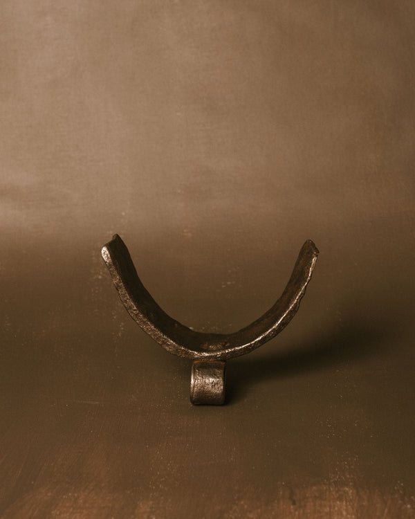 Horn-shaped found iron object with curved form and dark patina, displayed as a small sculptural piece.