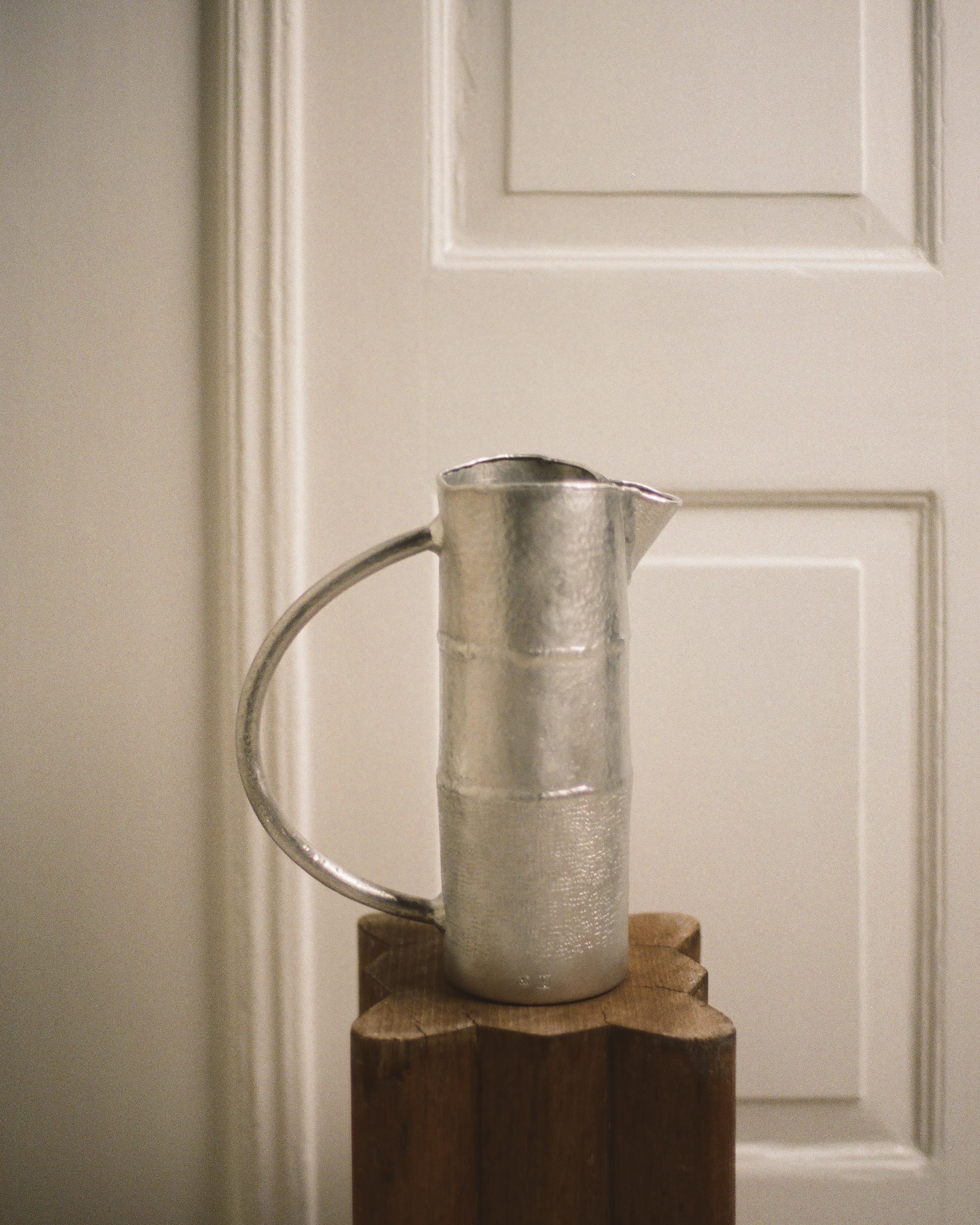 Metal pitcher on a wooden block against a neutral wall