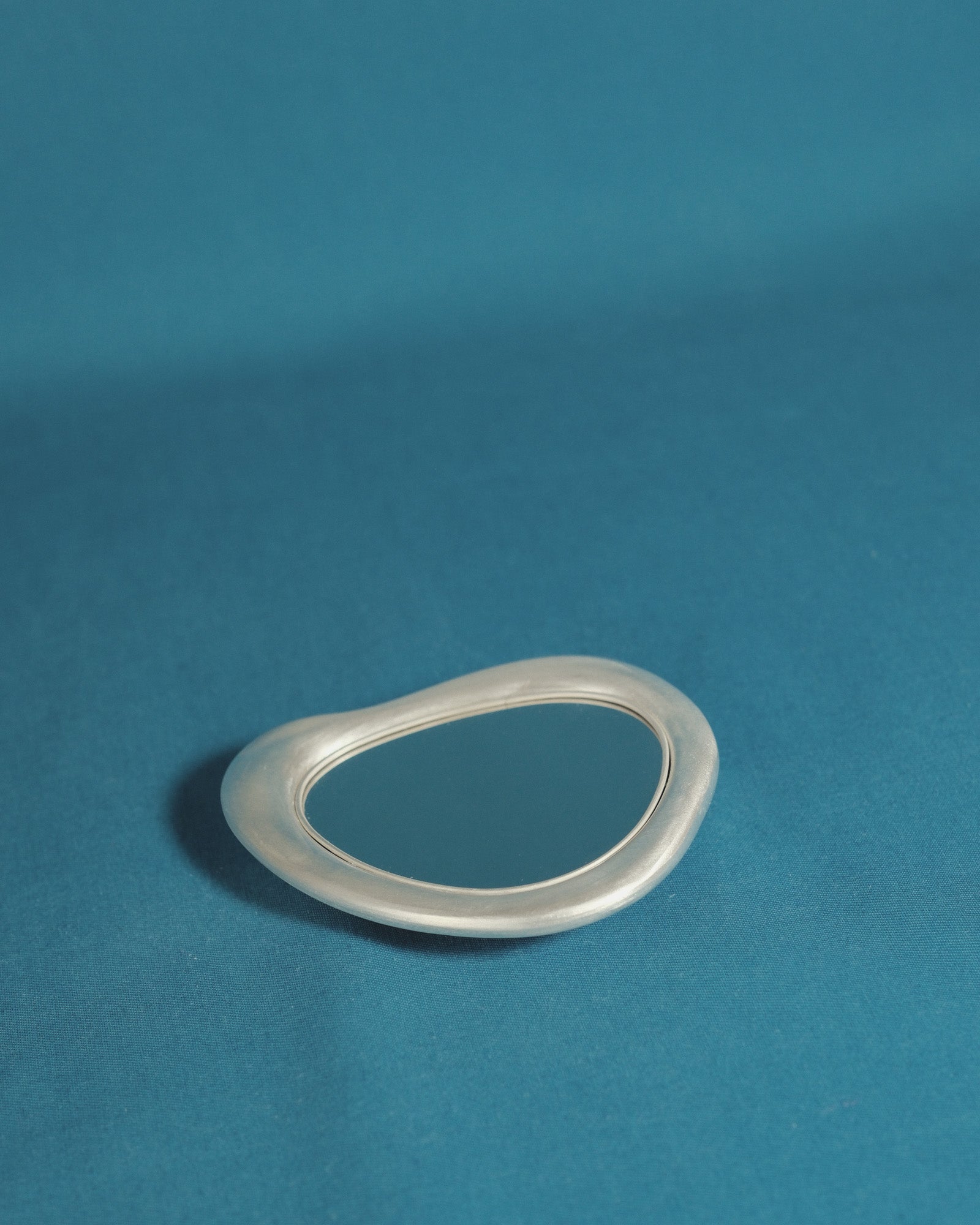 Christian+Jade Mirror silver-plated metal and polished stainless steel compact handheld object capturing reflection and trace of use.