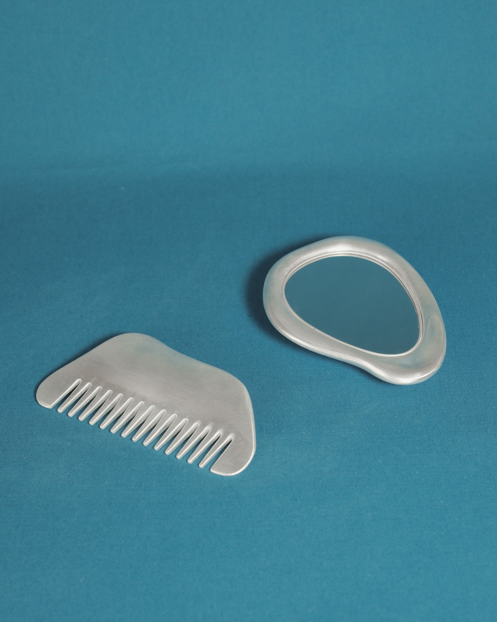 Christian+Jade Vanity Set mirror and comb cast in silver-plated metal and polished stainless steel with refined form and surface detail.