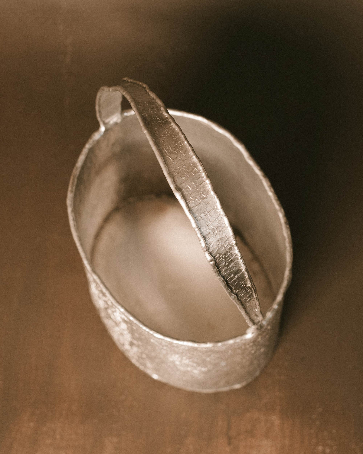 Curved handle of Basket 2, textured aluminum surface, angled view